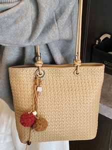 Brown woven tote bag for women featuring a plush ball charm and slim round handles