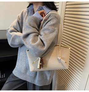 Close-up of beige leather tote bag featuring knot handle and decorative bead charms