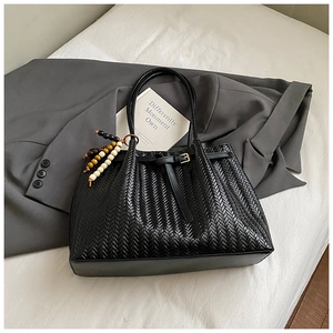 Detail of black woven tote bag with beaded charm and metal buckle on white fabric