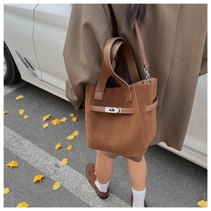 Brown faux suede bucket bag with metal twist lock shown in a stylish autumn outdoor setting