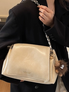 Minimalist beige chain shoulder bag with plush monster charm on black blazer