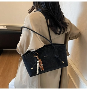 Detail of a black suede tote bag with ethnic wood bead pendant and slim rope shoulder strap