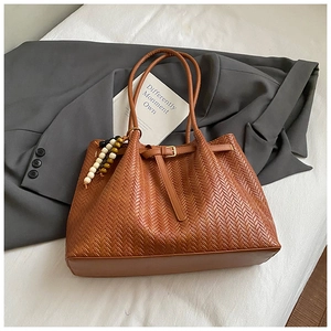 Detailed close-up of brown woven leather texture and elegant beaded charm on tote bag
