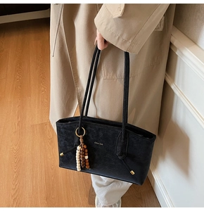 Close-up of black textured tote bag with wooden bead charm and long shoulder straps