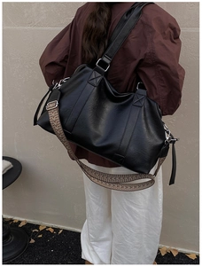 Close-up of black leather tote bag with stylish woven wide shoulder strap and metal hardware