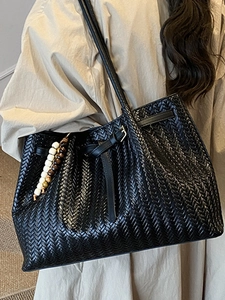 Minimalist black woven tote bag with leather strap and decorative beaded charm