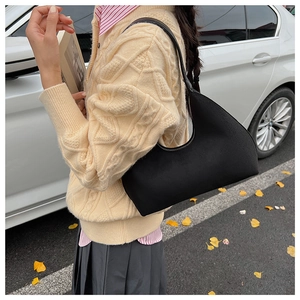 Outdoor street view of a black crescent underarm bag worn on shoulder by a model