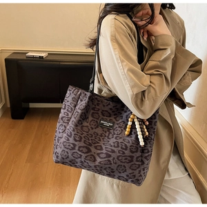 Detail view of leopard print tote bag featuring a leather logo tag and wooden bead charm