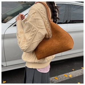 Brown suede underarm bag with minimalist arc design worn on shoulder in autumn setting