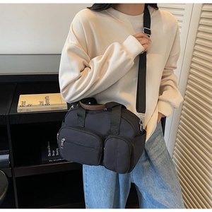 Detail view of a black multi-pocket nylon shoulder bag worn by a model in a library