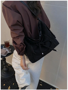 Détail du sac hobo en daim noir avec surpiqûres contrastées et nœud décoratif chic