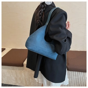 Blue suede hobo bag on shoulder showing its elegant half-moon shape and retro matte finish
