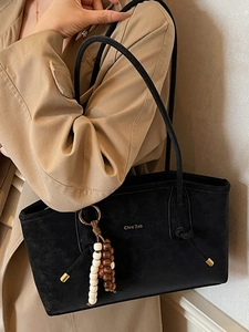 Minimalist black matte leather tote bag with wooden bead charm on a khaki trench coat model