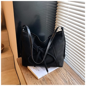 Détail d'un sac cabas en daim noir avec un grand nœud décoratif et des coutures blanches