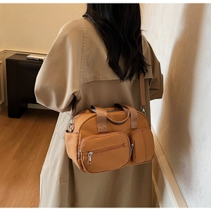 Model wearing a brown multi-pocket crossbody bag with wide strap in a minimalist room