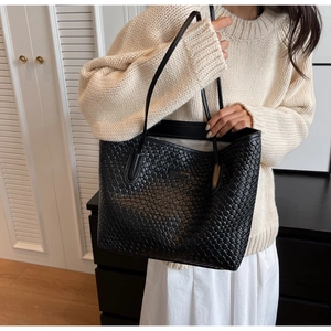 Close-up of black woven leather tote bag texture and logo plate in cozy home setting