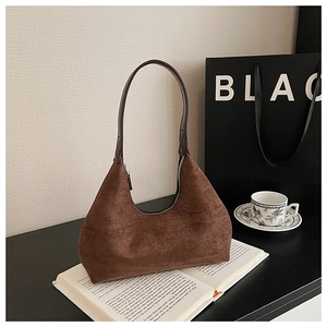 Close-up of brown suede hobo bag on book with minimal shopping bag and tea cup