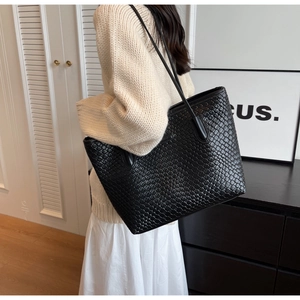 Detail of a large black woven leather tote bag shown from a side angle on a model
