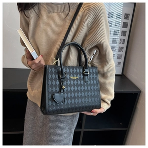 Detail of black quilted leather handbag featuring gold logo and heart-shaped pendant