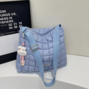 Close-up of light blue quilted shoulder bag with plush rabbit charm and wide strap
