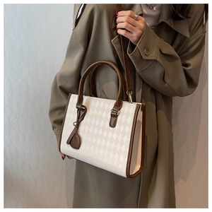 Close-up of cream quilted handbag with brown trim and gold fashion lettering