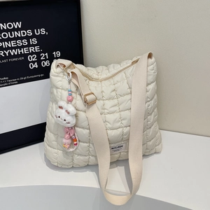 Detail of off-white quilted bubble bag featuring wide strap and cute plush rabbit charm