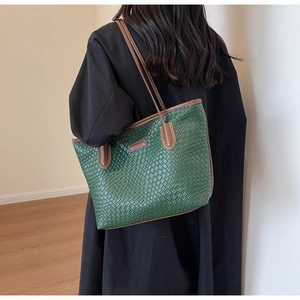 Detail of dark green embossed tote bag with brown leather handles and textured surface