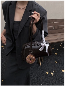 Detail view of dark brown leather handbag featuring lace ribbon and donut plush charm