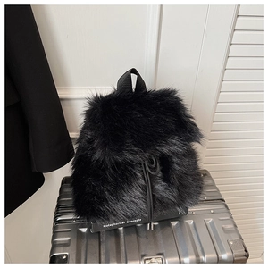 Détail d'un sac à dos en fausse fourrure noire duveteuse sur une valise argentée