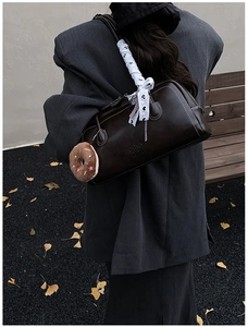 Detail of vintage brown leather Boston bag with white stitching and donut charm on shoulder