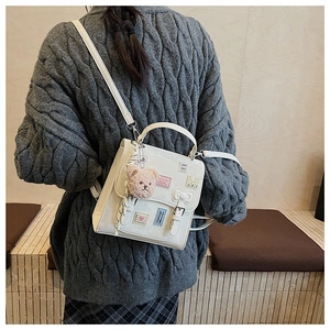 Detailed back view of a white leather bag with love patches and a plush bear charm
