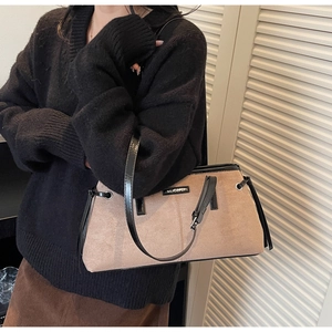 Detail of beige suede handbag featuring black leather trim and silver brand plate