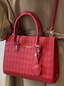 Minimalist red diamond quilted tote bag with heart pendant worn on a trench coat