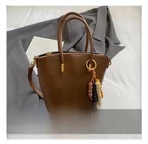 Close-up of brown faux leather tote bag featuring a beaded charm and golden zipper detail
