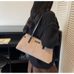Close-up of a brown suede tote bag with black leather straps and metal brand plate