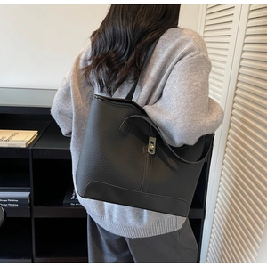 Détail d'un cabas en cuir grainé noir avec fermoir doré porté à l'épaule