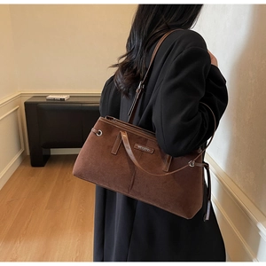 Detail of suede vintage brown shoulder bag showing metal logo and texture on model