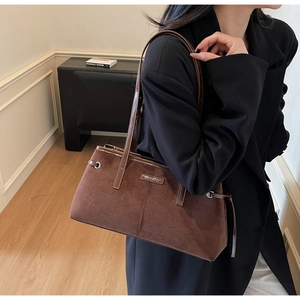 Close-up of brown suede shoulder bag with dual leather straps and gold logo detail