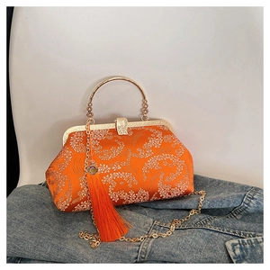 Detailed macro view of orange satin shell bag with white floral embroidery and tassel