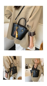 Detail of black bucket handbag showing fine texture, gold hardware, and colorful bead charm