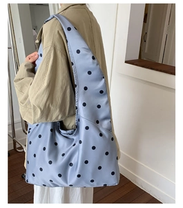 Detail der hellblauen Satin-Hobo-Tasche mit Punkten, getragen von einem Modell im Raum