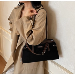 Detail of vintage black suede handbag featuring brown leather trim and metal logo