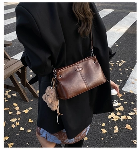 Detail of vintage brown leather crossbody bag with cute plush bear charm on autumn street