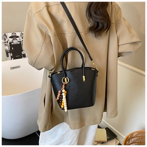 Lifestyle shot of black leather bucket bag with wood bead charm and golden hardware detail