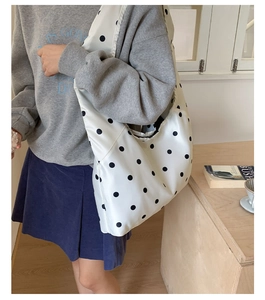 Detailansicht einer großen weißen Satin-Tasche mit schwarzen Punkten an einem Model