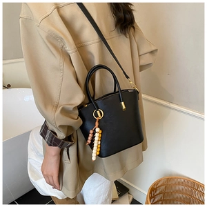 Detail of minimalist black bucket bag with leather texture and colorful beaded tassel charm