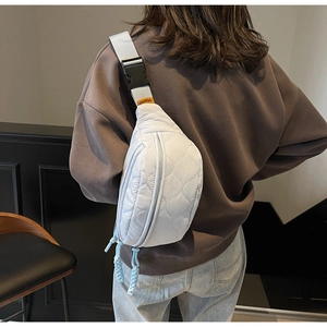 Detail der hellblauen Stepp-Brusttasche mit orangem Etikett und grauem Gurt am Model