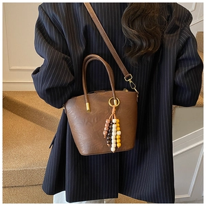 Detail of a dark brown leather bucket bag with ethnic beaded charm and golden hardware