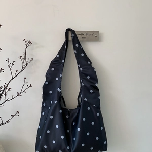 Detailansicht der schwarzen Satin-Tragetasche mit weißen Punkten und breitem Schultergurt