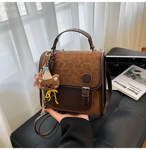 Close-up of vintage leopard print crossbody bag with bear charm on a dark leather stool
